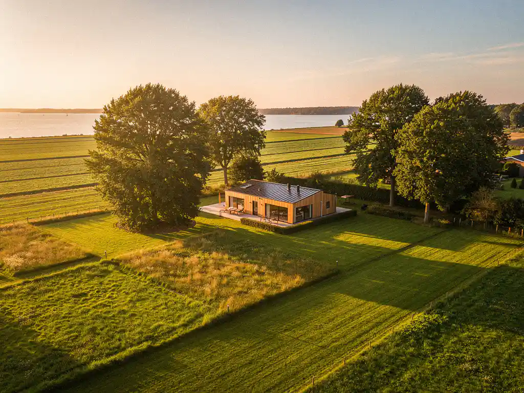 Luchtfoto van een zonnig vakantiepark in Zeeland met een chalet tussen volwassen bomen en verzorgde groene percelen.